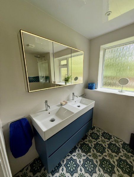 Bathroom design and installation by Richard & Richard’s, featuring a double basin vanity, blue fitted bathroom furniture, illuminated mirrored cabinet and patterned floor tiles. Designed, supplied and installed from our Stockport showroom.