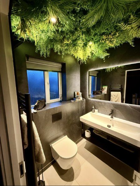 Cloakroom and bathroom design by Richard & Richard’s, featuring dark stone-effect wall tiles, a wall-hung WC, black vanity unit, illuminated mirror, black brassware and a feature planted ceiling. Designed, supplied and installed from our Stockport showroo