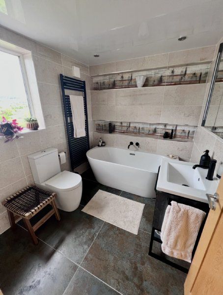 Bathroom design and installation by Richard & Richard’s, featuring a freestanding bath, black brassware, black heated towel rail, stone-effect wall tiles, feature tile detailing and dark floor tiles. Designed, supplied and installed from our Stockport sho