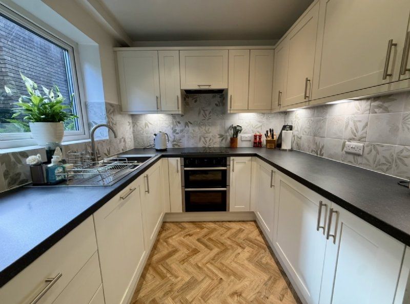 Kitchen design and installation by Richard & Richard’s, featuring classic shaker-style kitchen doors, black worktops, patterned splashback tiles, under-cabinet lighting and wood-effect herringbone flooring. Designed, supplied and installed from our Stockp