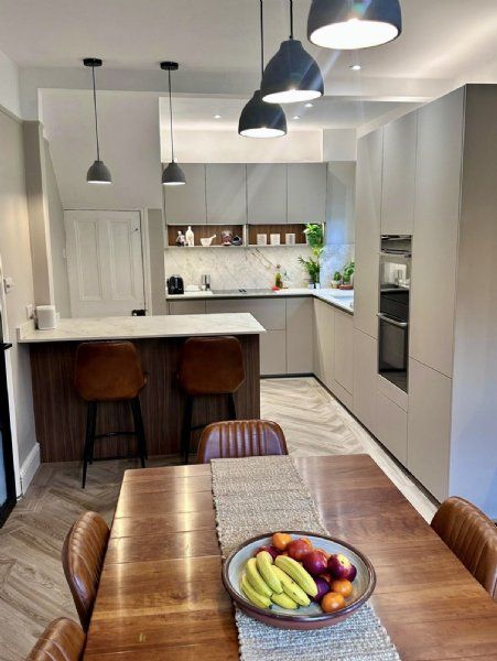 Open-plan kitchen design and installation by Richard & Richard’s, featuring handleless fitted kitchen furniture, marble-effect worktops and splashback, integrated appliances, breakfast bar seating, open shelving and herringbone flooring. Designed, supplie